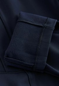 Navy blue urheiluasu, jossa on sileä pinta ja ommeltuja yksityiskohtia, ja jossa on taitettu hiha lisää mukavuutta varten.