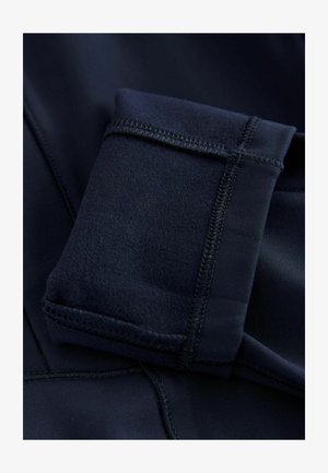 Tumesinise sinine sportlik rõivas sileda tekstuuriga ja õmmeldud detailidega, millel on volditud varrukas lisafunktsionaalsuse saavutamiseks.