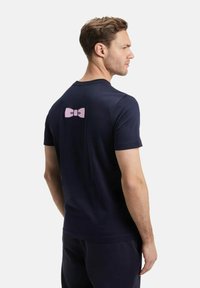 T-shirt navy à manches courtes en tissu doux, avec un graphique de nœud rose au dos, un col rond et une coupe décontractée.
