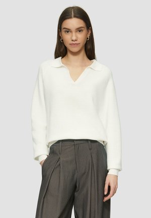 Witte geribbelde pullover met een V-hals en kraag, met lange mouwen. Gecombineerd met grijze broek met krijtstrepen; beide kledingstukken hebben een ontspannen pasvorm.