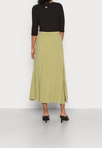 Zwarte geribbelde top met driekwart mouwen, gecombineerd met een lange, lichtgroene, luchtige rok met een zijsplit, gedragen met zwarte sandalen met hakken.