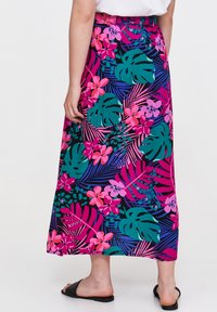 Kwiatowa maxi spódnica w kolorach różowym, zielonym i granatowym z tropikalnymi wzorami liści i kwiatów; gładki materiał; prosty krój. Noszona z czarnymi klapkami.
