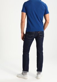 Blue short-sleeve polo shirt, dark denim jeans, white sneakers. Noticeable stitching on jeans, fitted design, and cuffed hem.