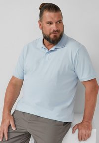 Jasnoniebieska koszula polo z oddychającego materiału, z krótkim rękawem, dwoma guzikami przy kołnierzyku oraz dyskretnym haftem logo na piersi.