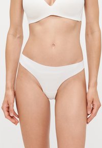 Witte stringonderbroek gemaakt van soepele stof, met een low-rise tailleband en naadloze randen voor een minimalistisch ontwerp.
