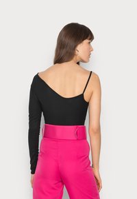 Bodysuit preto com textura canelada, um dos mangas longas e um lado desalojado, combinado com calças rosa de cintura alta com um cinto largo.