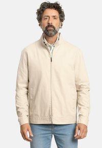 Chaqueta de mezcla de algodón en color beige con cuello alto, cremallera frontal y bolsillos laterales. Presenta una textura suave y un diseño minimalista.