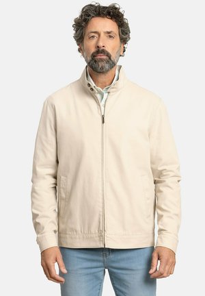 Chaqueta de mezcla de algodón en color beige con cuello alto, cremallera frontal y bolsillos laterales. Presenta una textura suave y un diseño minimalista.
