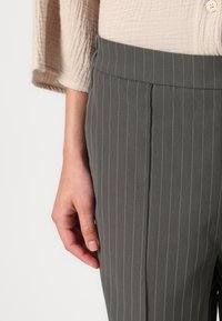 Sive pinstripe hlače iz gladkega, lahkega materiala, z natančno prilegajočim krojem in ravnim pasom, v kombinaciji z teksturirano bež majico.