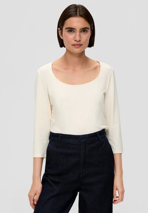 Crème lange mouw top met een brede ronde halslijn, gecombineerd met donkerblauwe hooggeknoopte broek. Soepele textuur en aansluitend ontwerp.