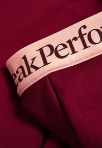 Bordeaux sportstof met een lichtroze tailleband waarop de tekst "Peak Performance" in donkerbruin staat. Soepele textuur met stikdetails.