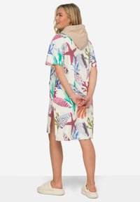 Huppari mekko kevyestä kankaasta, jossa on värikäs merieläinkuvio. Lyhyet hihat, sivuhalkiot ja beige huppu korostavat mekkoa.