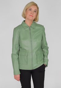 Groene leren jas met een kraag, voorkeursrits en twee voorzakken, gecombineerd met zwarte broek. Glad textuur, getailleerd ontwerp.