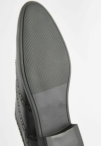 Suela de zapato de cuero negro con agarre de goma texturizada. Presenta un acabado suave y un diseño de perfil bajo, adecuado para ropa formal.