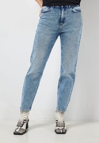 Lichtblauwe denim jeans met een rechte pijp stijl, voorzien van vijf zakken en subtiele vervaging. Gecombineerd met gepatternde enkellaarsjes.