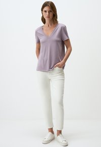 T-shirt V-neck a maniche corte di un delicato lilla, con una vestibilità comoda, abbinata a jeans bianchi alla caviglia e sneakers bianche.