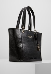 Sac fourre-tout en similicuir noir avec texture crocodile. Comprend une quincaillerie dorée, deux poignées et un charme décoratif.