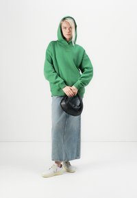 Grønn hettegenser, denim maxiskjørt, svart håndveske og hvite joggesko med beige detaljer; avslappet passform, teksturert stoff, enkelt design.