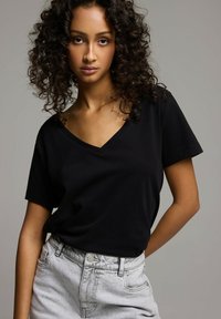 Czarny t-shirt z dekoltem w serek, wykonany z miękkiego materiału, z krótkimi rękawami, w połączeniu z jasnoszarymi dżinsowymi szortami z wysokim stanem, o minimalistycznym wzornictwie i kroju.