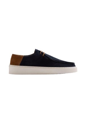 Zapato casual de ante azul marino para hombre con parche marrón en el talón, cordones color marrón claro, suela blanca y costura estilo mocasín en la puntera.