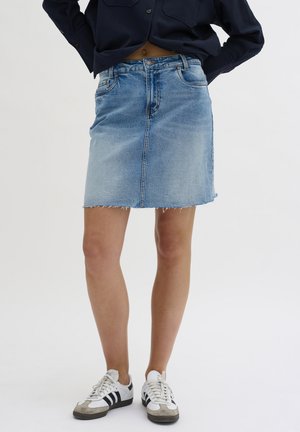 Denim skirt in light blue, knee-length with frayed hem. Features front pockets and a zip fly. Paired with black and white sneakers.