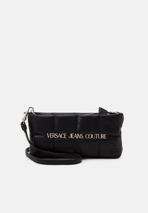 Czarna pikowana torebka na nadgarstek z srebrnym napisem "Versace Jeans Couture" i odpinanym paskiem na białym tle.