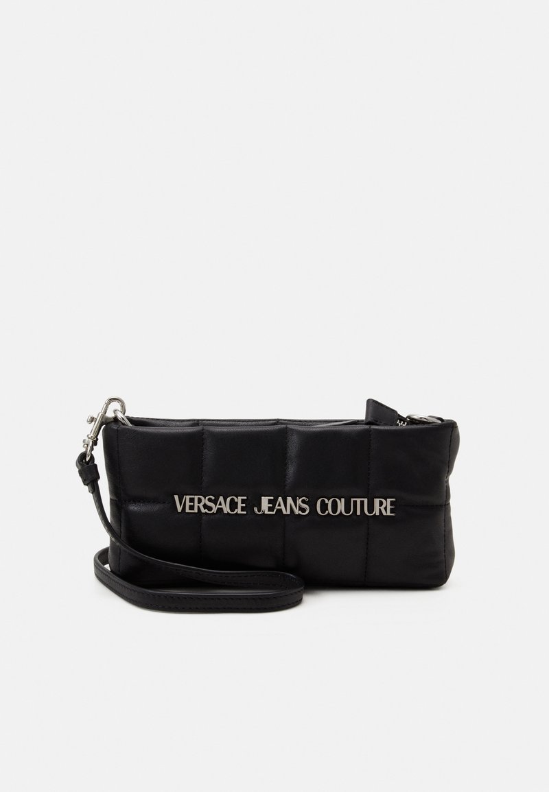 Petit sac bracelet noir matelassé avec lettrage argenté "Versace Jeans Couture" et bandoulière amovible sur fond blanc.