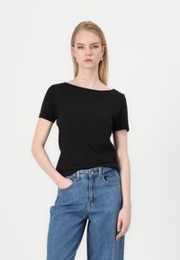 Svart kortärmad topp med båtringning, tillverkad av mjukt material. Kombinerad med högmidjade blå denimjeans. Enkel och minimalistisk design.