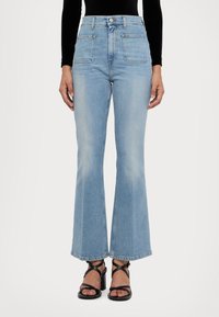 Vaqueros acampanados de talle alto en denim azul claro, con bolsillos delanteros, textura deslavada y corte recto en la parte inferior. Sandalias negras con tiras.