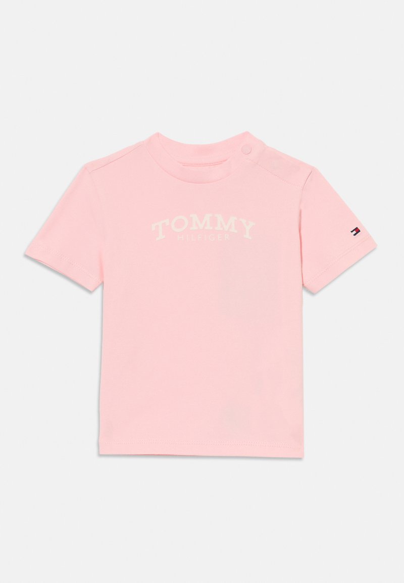 Hele roosa lühikeste varrukatega t-särk, mis on valmistatud pehmest puuvillast. Omab ümarat kaelust, õlavarre nupu detaili ja trükitud valget "TOMMY HILFIGER" logo.