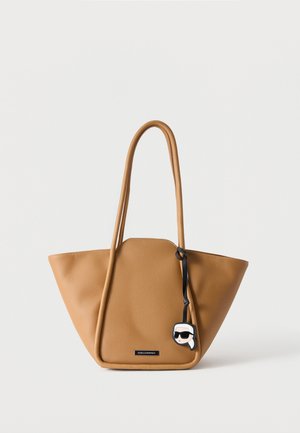 Sac cabas en cuir couleur tan avec longues anses et petit porte-bonheur cartoon représentant un visage avec des lunettes de soleil, sur fond blanc uni.
