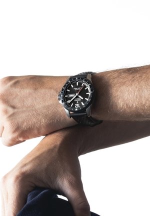 Black analog wristwatch with a round case, contrasting white markings, and a textured rubber strap. Display shows the date and day.