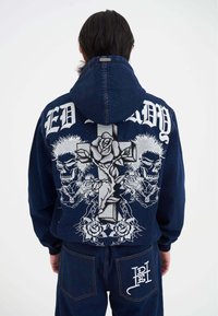Der Denim-Hoodie hat ein silbernes grafisches Design von Totenköpfen und Rosen, das auf einem Kreuz überlagert ist. Er verfügt über eine Kapuze und den Text "ED HARDY" oben.