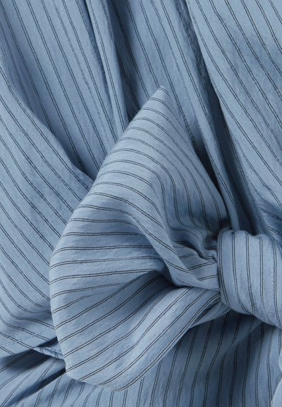 Tissu bleu avec de fines rayures verticales noires noué en un nœud lâche, mettant en valeur les plis et la texture.