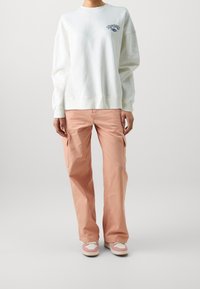 Biała bluza z długimi rękawami i okrągłym dekoltem, zestawiona z jasnoróżowymi spodniami cargo z bocznymi kieszeniami i luźnym krojem. Casualowe trampki.