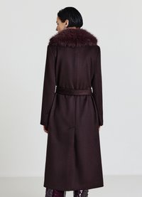 Cappotto in lana borgogna con colletto in pelliccia sintetica, maniche lunghe, vita cinturata e vestibilità sartoriale, mostrato da dietro con una texture liscia.