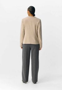 Beiger taillierter Blazer mit langen Ärmel, kombiniert mit grauen weiten Hosen, die eine glatte Textur und einen geraden Schnitt aufweisen.