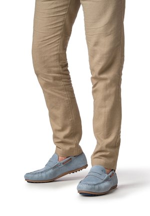 Mocassins en daim bleu clair avec des détails cousus et des accents marron, portés avec un pantalon beige slim, illustrant un look décontracté.