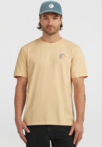 Lys ferskenfarvet bomulds T-shirt med korte �ærmer og rund hals, prydet med et cirkulært logo i blå og orange på venstre brystområde.