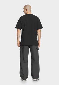 Czarny, oversize T-shirt z krótkimi rękawami, zestawiony z szarymi spodniami cargo z kieszeniami. Materiał wydaje się miękki i casualowy.