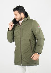 Veste parka zippée vert olive avec une capuche doublée en fausse fourrure, poches latérales et une poche poitrine ; présente un logo cousu sur la manche.