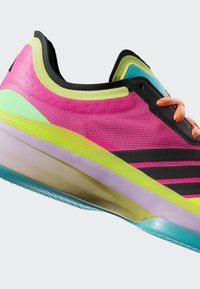 Kirkkaan pinkki ja neonvihreä urheilukenkä oransseilla nauhoilla, mustilla yksityiskohdilla ja sinivihreällä pohjalla, esitetty vinosta sivukulmasta.