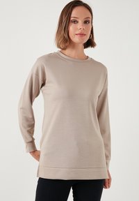 Felpa beige a maniche lunghe con scollatura a girocollo e aperture laterali. Tessuto morbido con vestibilità comoda, dotata di polsini e orlo a coste.