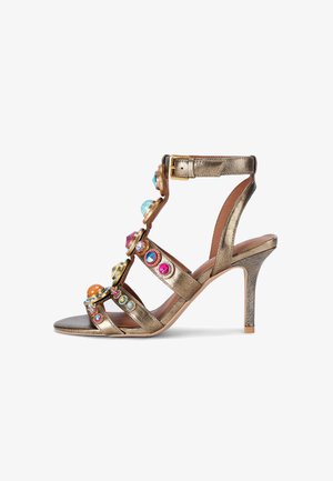 Sandal con tacco alto in metallo dorato, adornato con gemme multicolori, con punta aperta e cinturino alla caviglia regolabile. Texture liscia simile alla pelle.