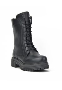 Botín de cuero negro hasta el tobillo con punta redonda, cierre de cordones y suela de goma gruesa. Presenta detalles de costura y un emblema de logo en el lateral.