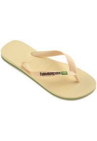 Tongs en caoutchouc beige avec semelle texturée et fines bretelles. Présente des rayures vertes, jaunes et bleues le long de la semelle. Logo Havaianas affiché.