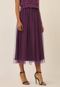 Gonna midi in tulle viola con texture a pois, vita elastica, design a strati, abbinata a tacchi alti neri con cinturini.