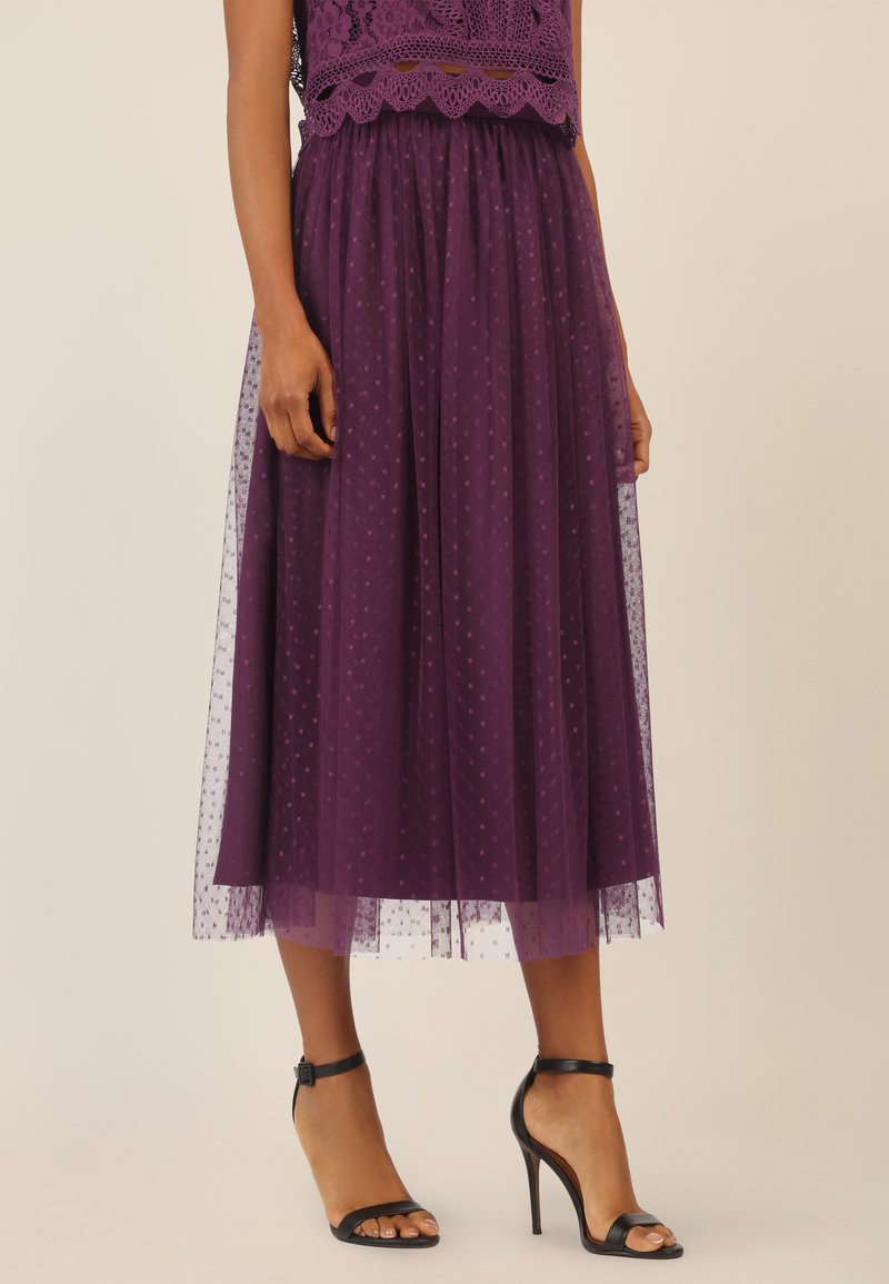 Gonna midi in tulle viola con texture a pois, vita elastica, design a strati, abbinata a tacchi alti neri con cinturini.