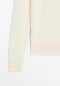 Manica di un maglione lavorato a maglia color crema con polsini a costine. Texture morbida, design minimalista, senza motivi o hardware visibili. Semplice ed elegante.