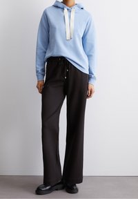 Felpa blu chiaro con lacci bianchi, abbinata a pantaloni sportivi neri. Scarpe nere completano l'outfit. Tessuto morbido, vestibilità rilassata.